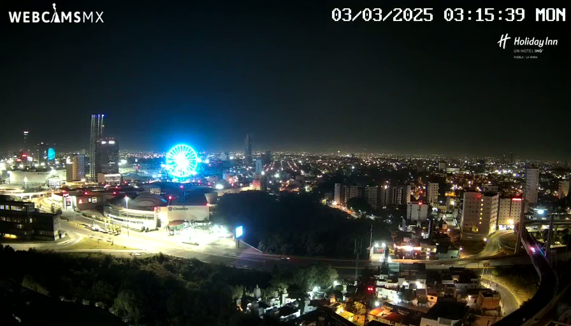 A nighttime view of a city illuminated with lights, featuring a Ferris wheel and several tall buildings, under a clear sky.
