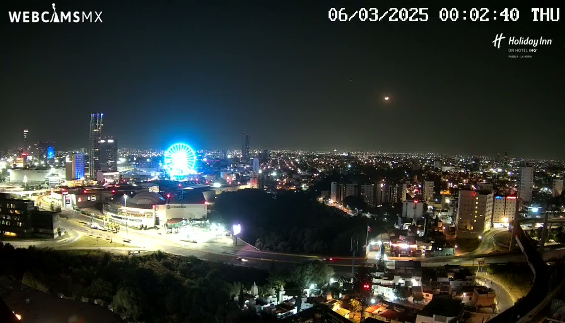 A nighttime cityscape with a brightly lit Ferris wheel and a sprawling city illuminated under a clear, dark sky.