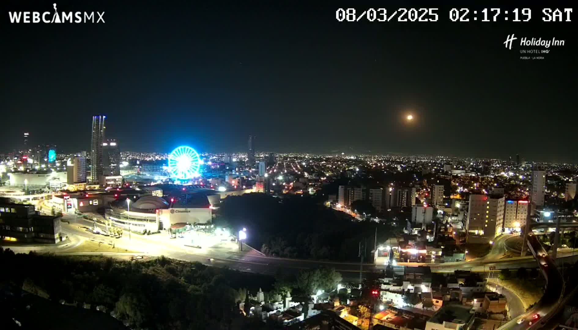 A nighttime cityscape with a Ferris wheel and illuminated buildings under a clear, moonlit sky.