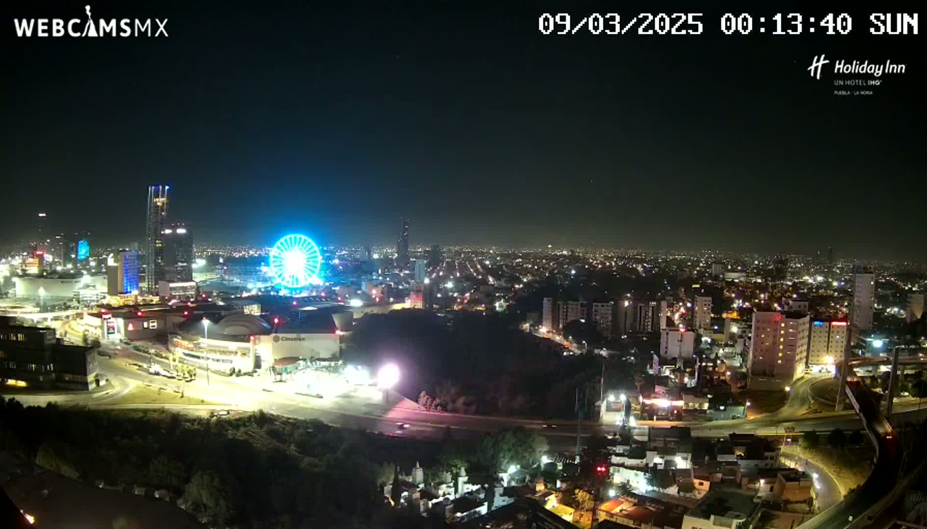 A nighttime, clear-sky view of a city illuminated with lights, featuring a Ferris wheel and several high-rise buildings.
