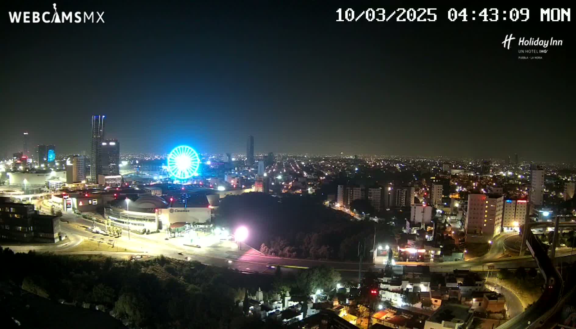 A nighttime cityscape with a Ferris wheel illuminated, under clear skies.