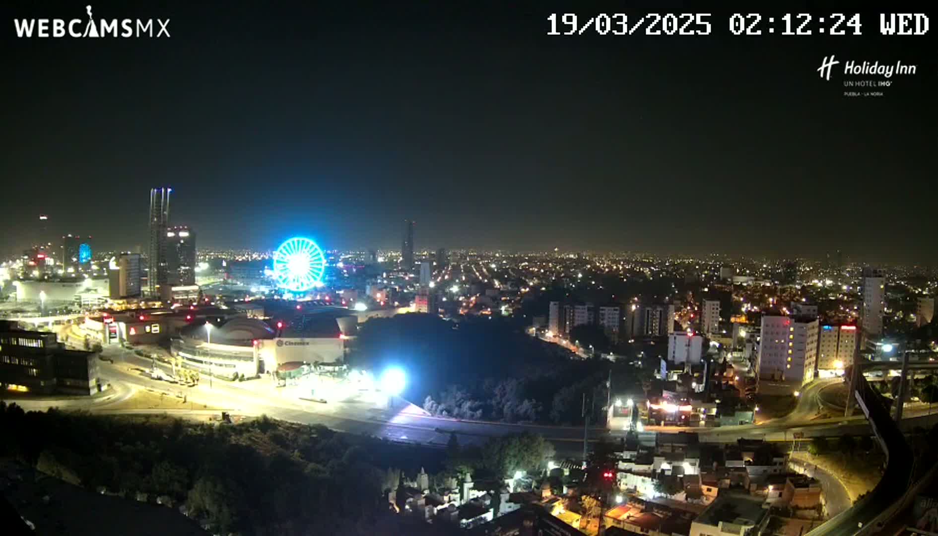 A nighttime, clear-weather view of a city skyline, featuring a brightly lit Ferris wheel and surrounding urban development.