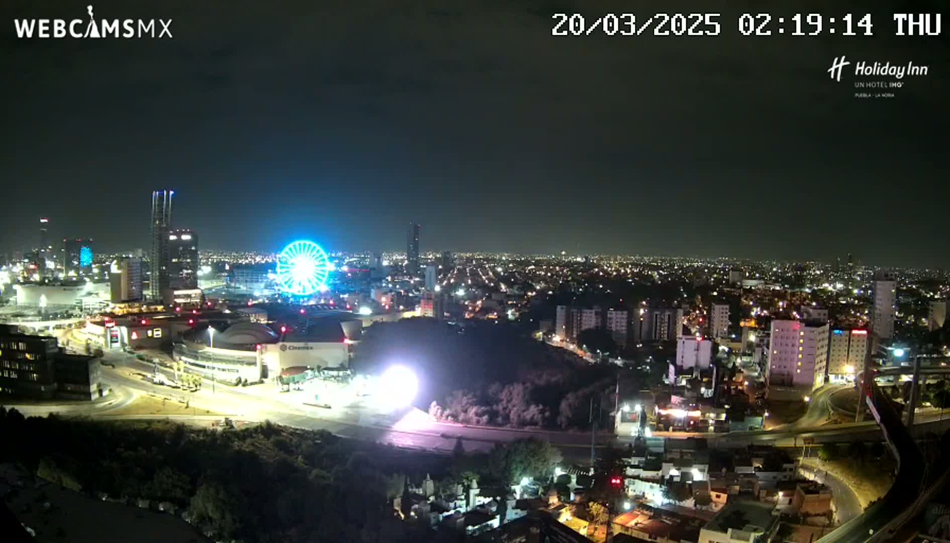 A nighttime aerial view of a city with a Ferris wheel illuminated, featuring a clear sky.