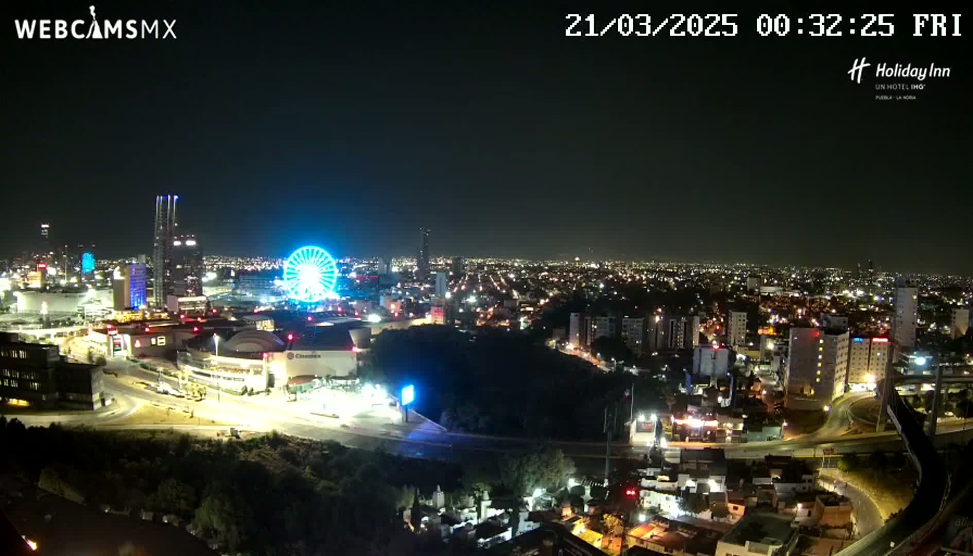A nighttime, illuminated cityscape with a Ferris wheel and a large entertainment complex is seen under a clear sky.