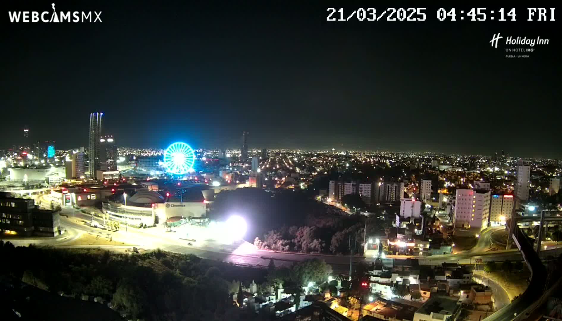 A nighttime, clear-weather view of a city skyline featuring a brightly lit Ferris wheel and surrounding buildings and roads.