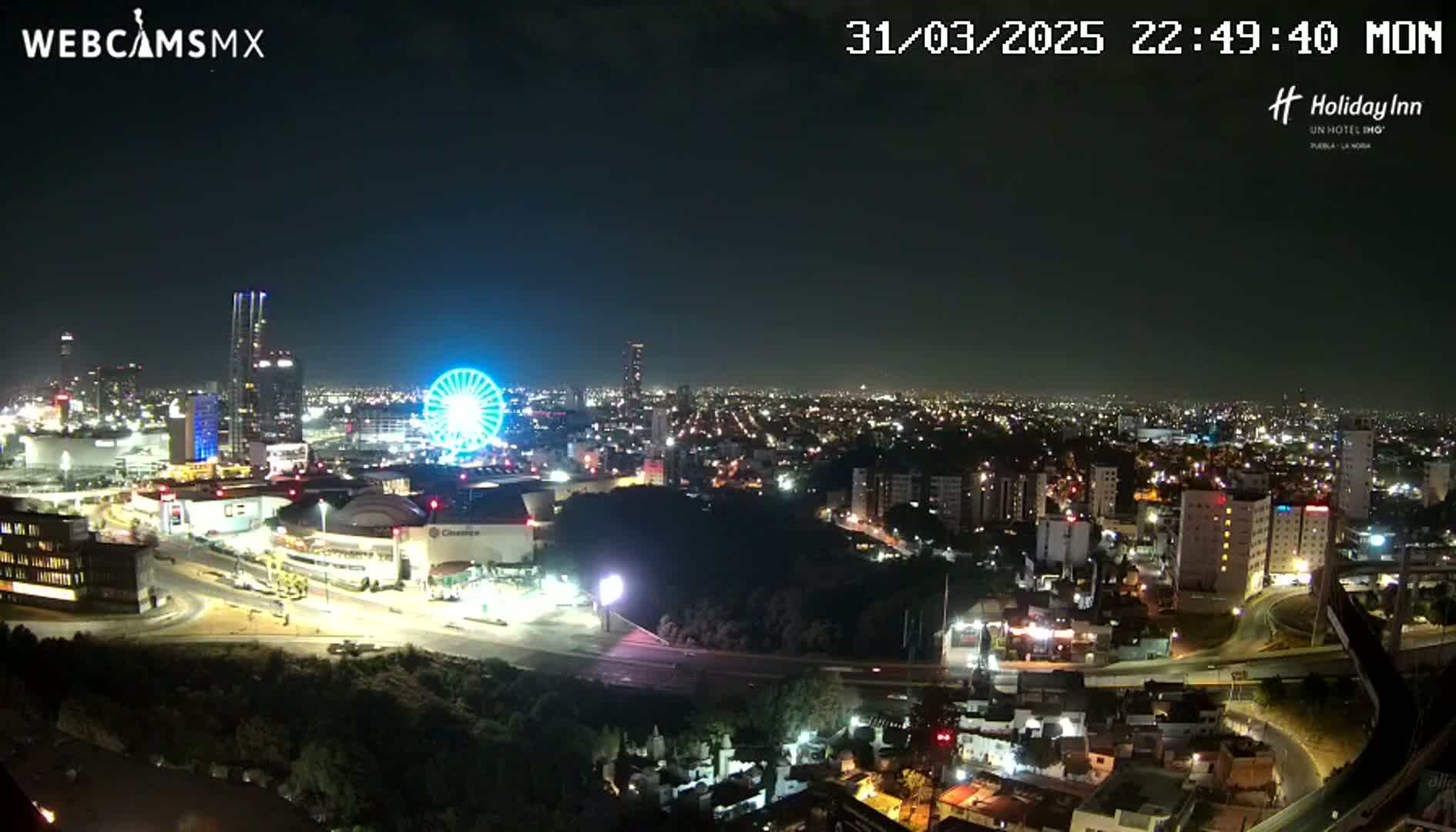 A nighttime view of a city with a Ferris wheel and numerous buildings illuminated, under a clear sky.