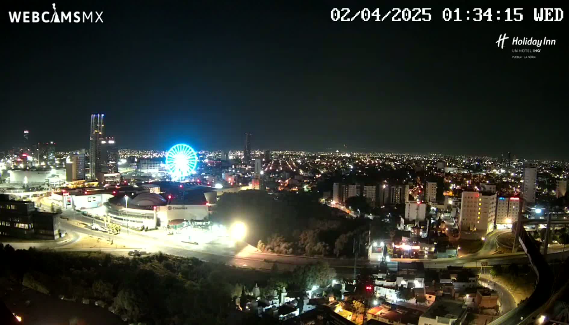 A nighttime, aerial view of a city with a Ferris wheel and several buildings illuminated, under a clear sky.