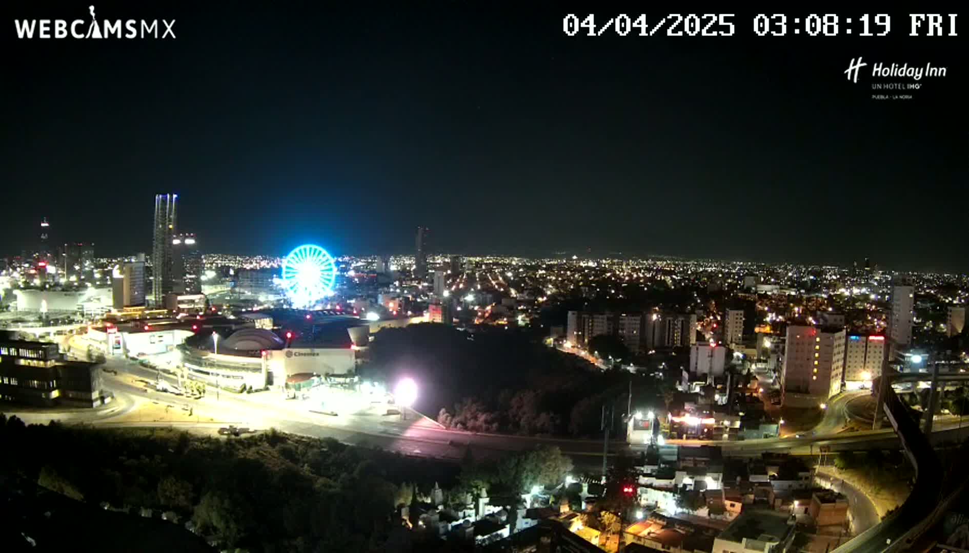 A nighttime view of a city with a Ferris wheel and illuminated buildings, under clear skies.