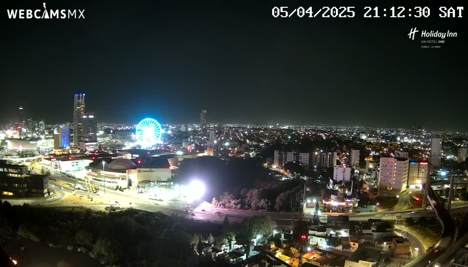 A nighttime view of a city with a Ferris wheel and illuminated buildings, under a clear sky.