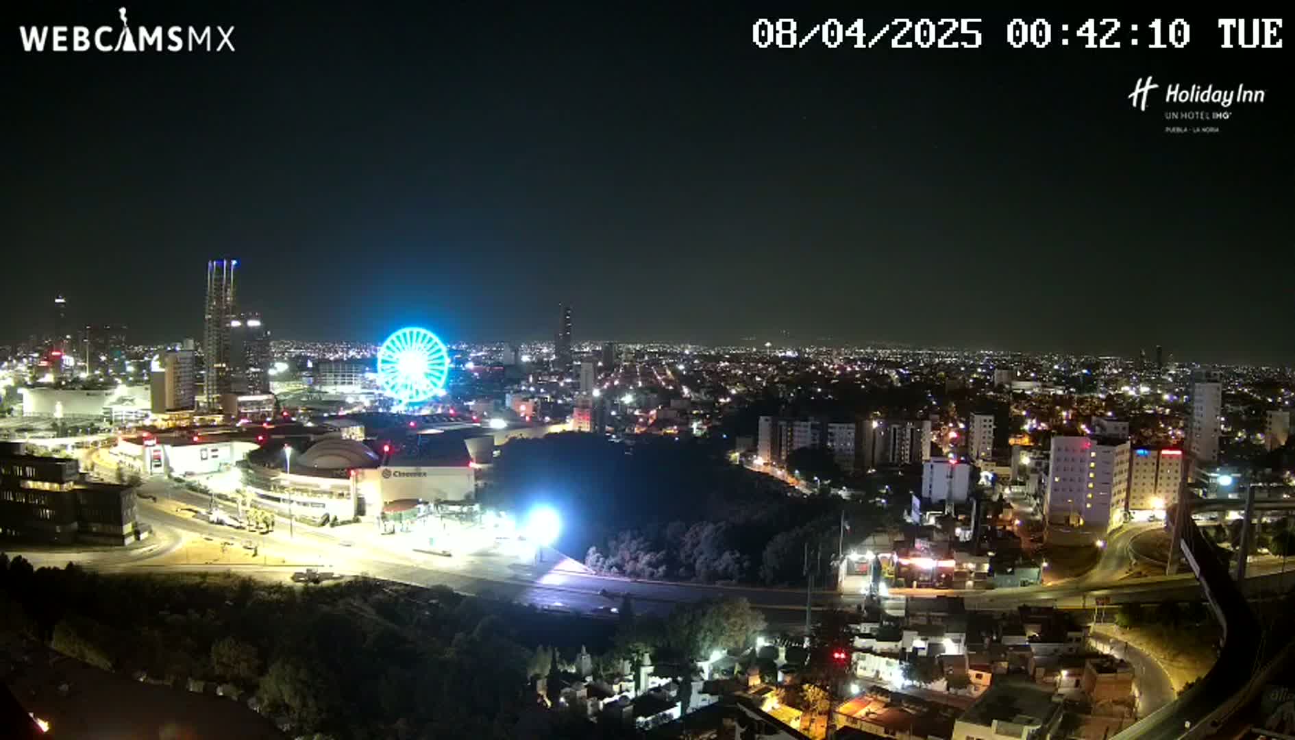 A nighttime aerial view of a city with a Ferris wheel and brightly lit buildings and roads.