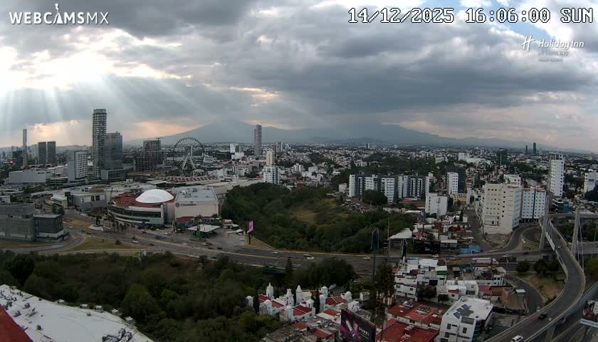 An expansive nighttime view captures a brightly lit city featuring numerous buildings, a prominent domed arena, and a large illuminated Ferris wheel under a clear night sky.