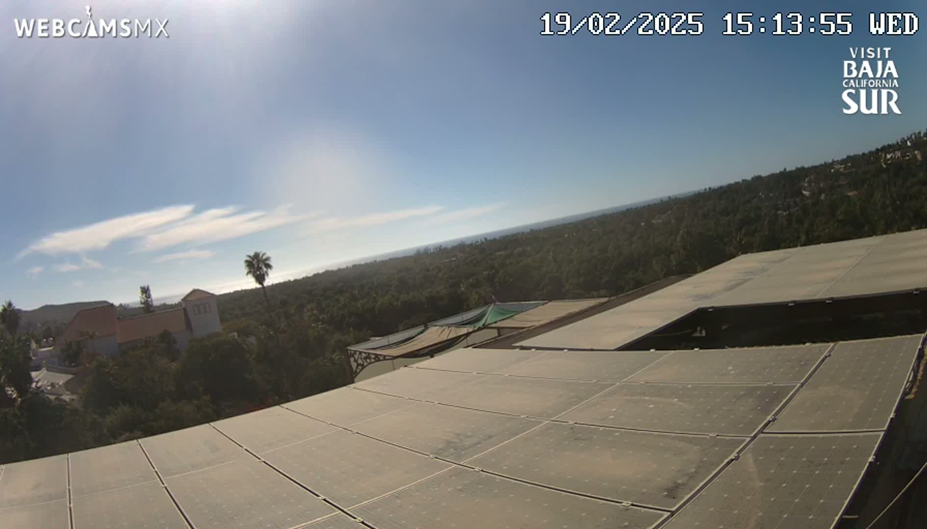A mostly sunny day overlooking a sprawling landscape of trees and buildings, partially obscured by a large solar panel array in the foreground.