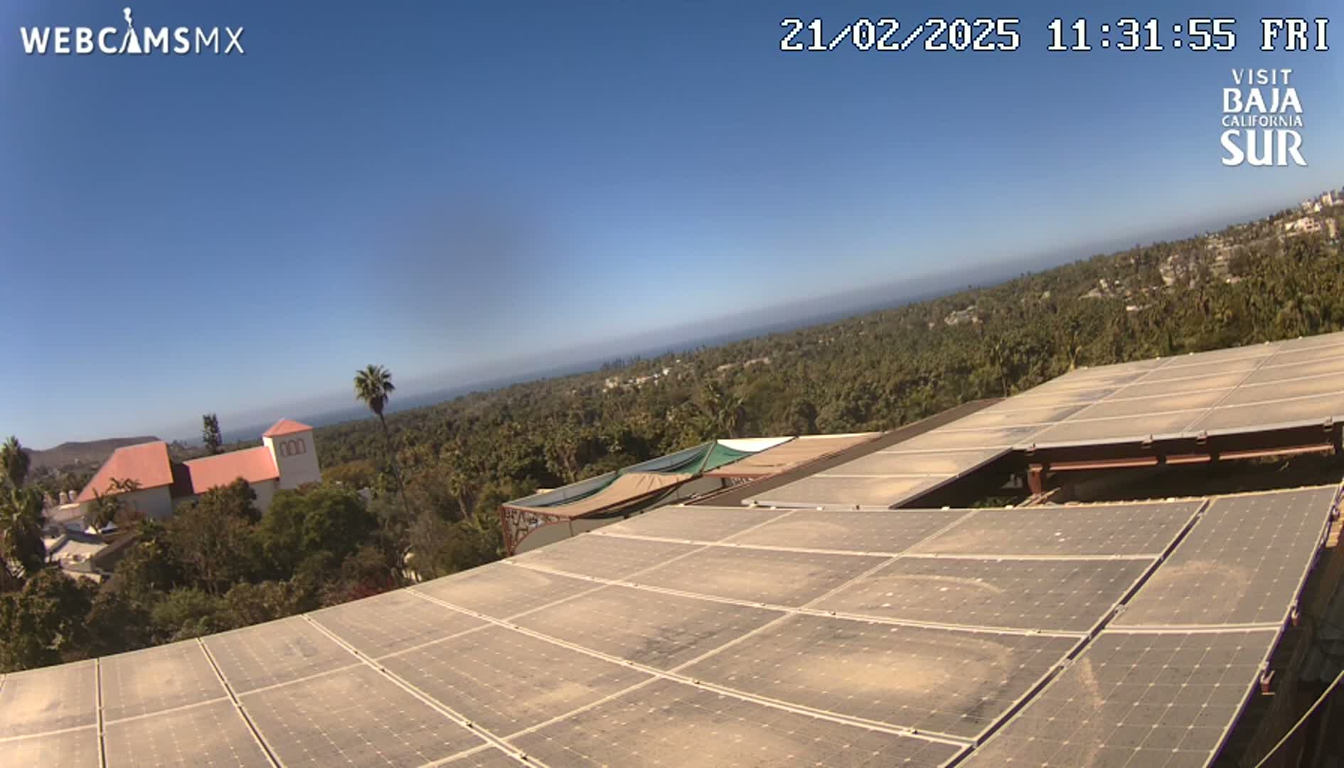 A large solar panel array sits atop a building overlooking a clear, sunny day with a distant ocean and lush green landscape.