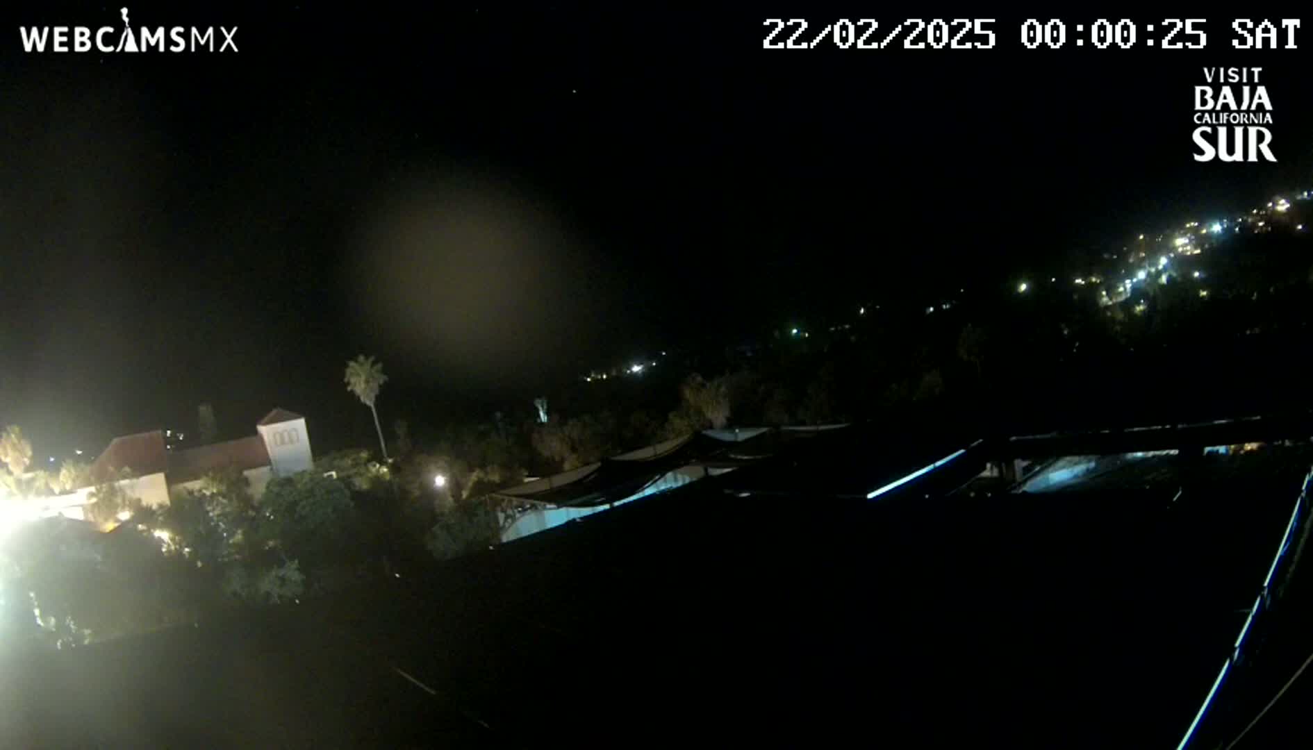 A nighttime, long shot of a building complex and surrounding vegetation under a clear sky.