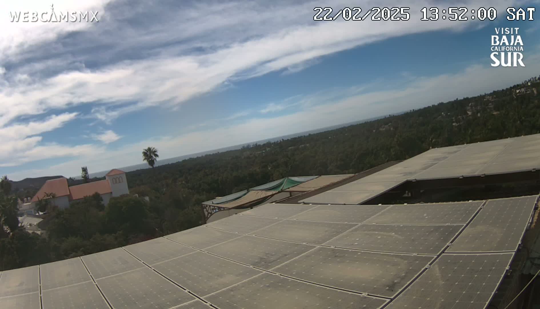 A partly cloudy sky overlooks a landscape of trees, buildings, and a large expanse of solar panels.
