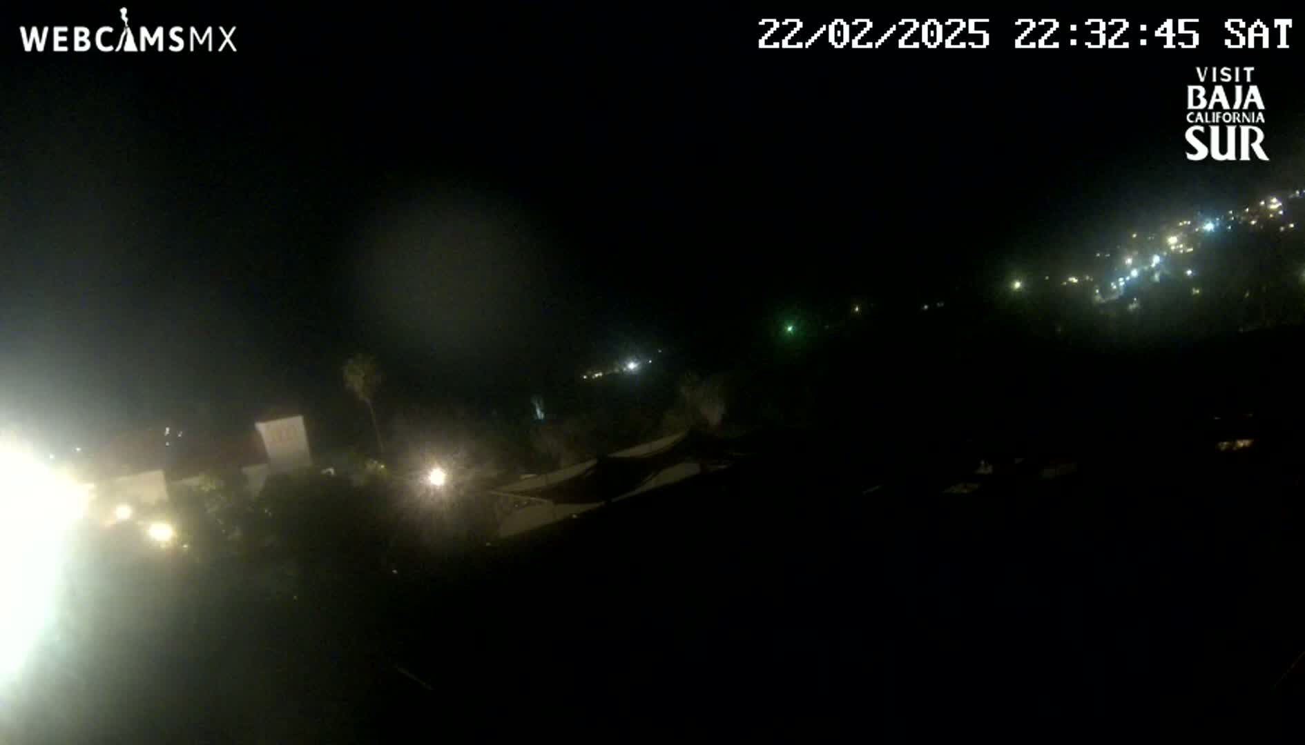 A nighttime, hazy view shows dimly lit buildings and distant lights from a town under a dark sky.