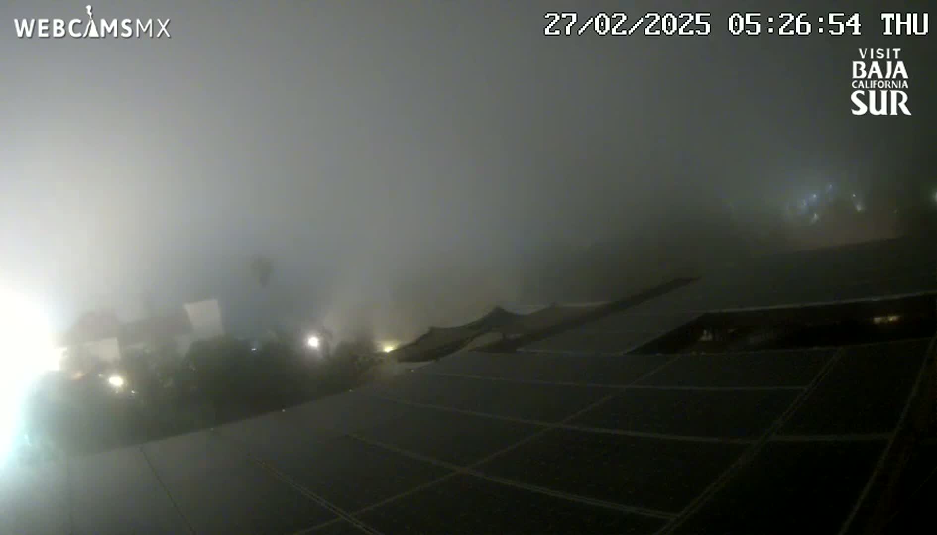 A nighttime view of a building's rooftop solar panels shrouded in thick fog.