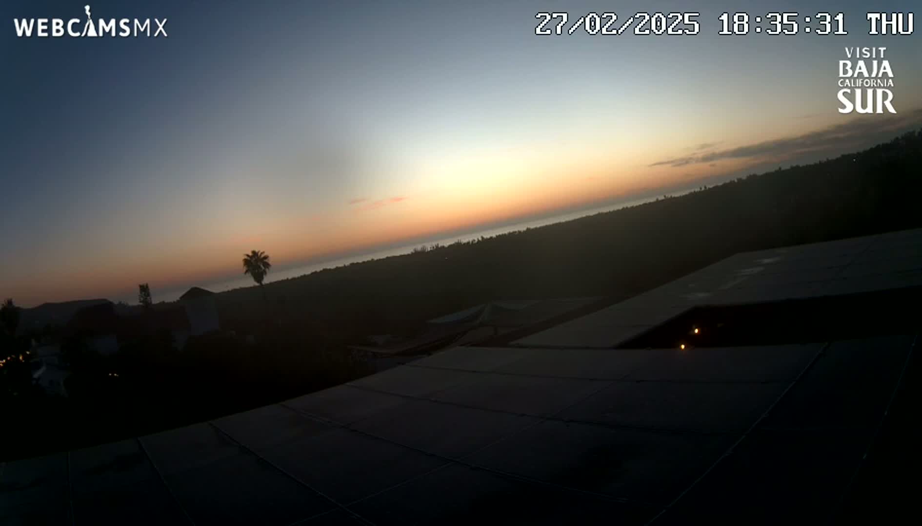 A sunset over a dark, silhouetted landscape is viewed from a rooftop.