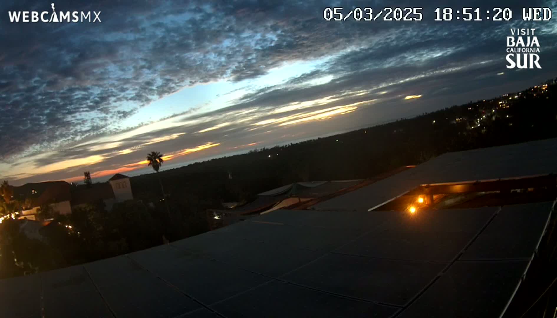 A twilight sunset with partly cloudy skies is seen from a rooftop overlooking a town at night.