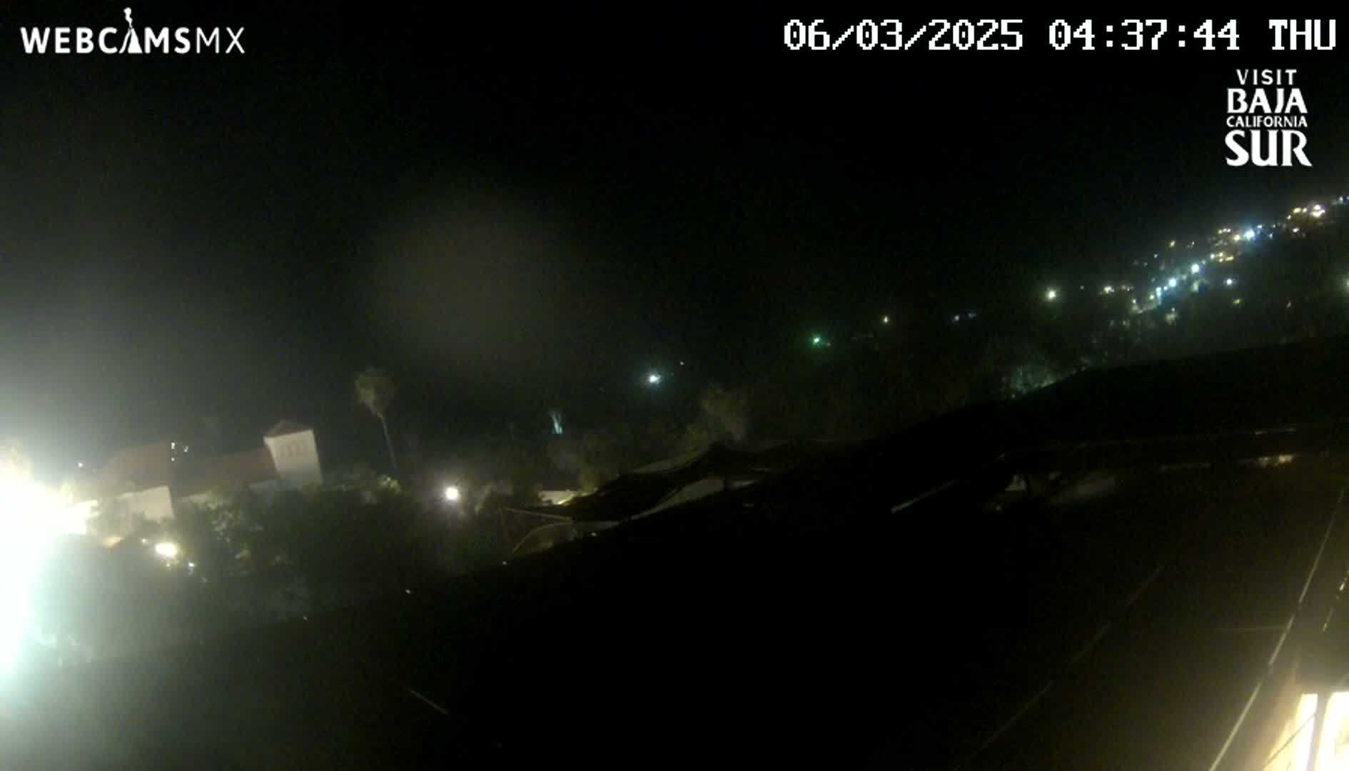 A nighttime, hazy view of a town with scattered lights, partially obscured by darkness.