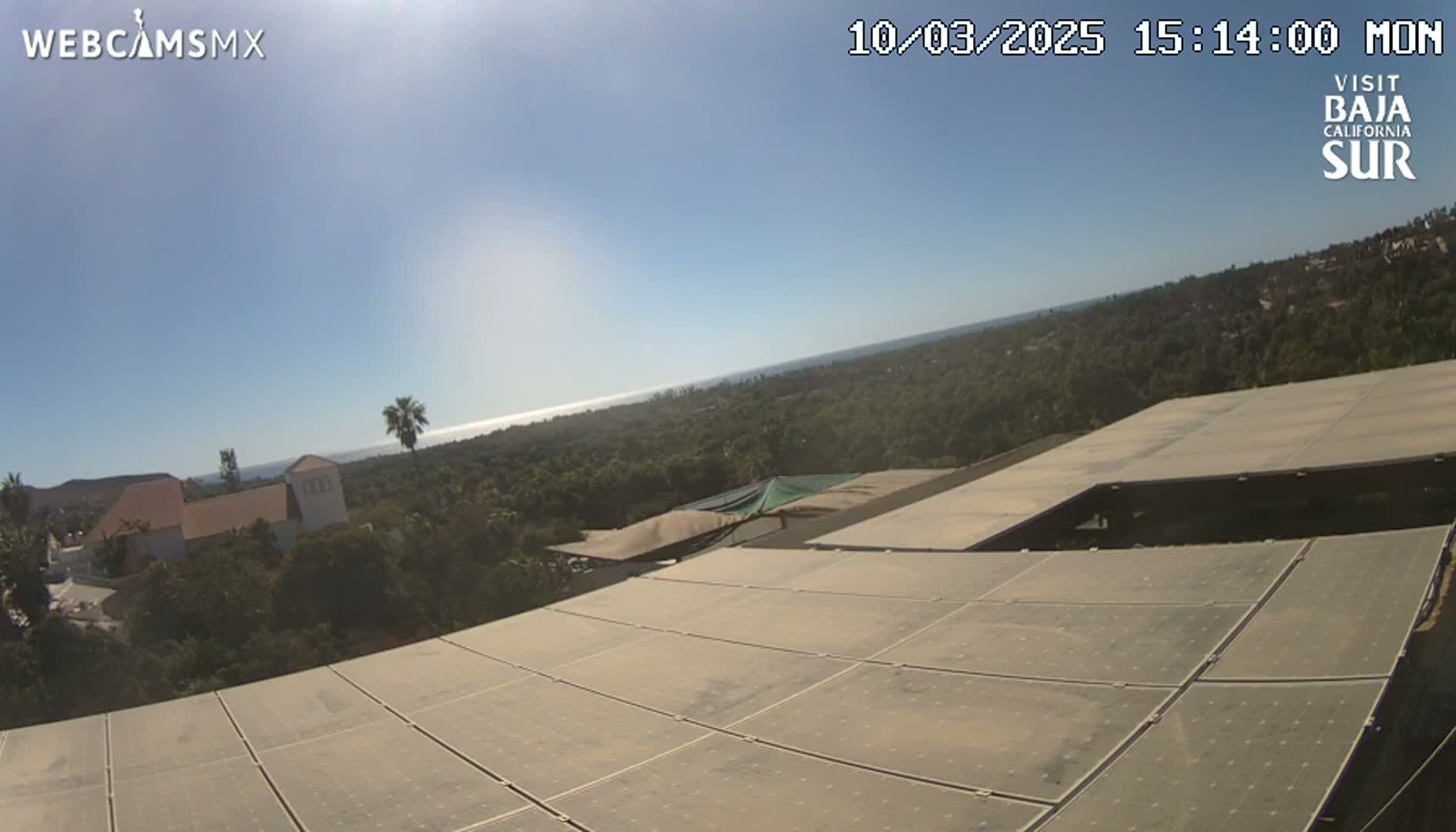 A large solar panel array is positioned atop a building overlooking a sunny ocean vista and lush green landscape.