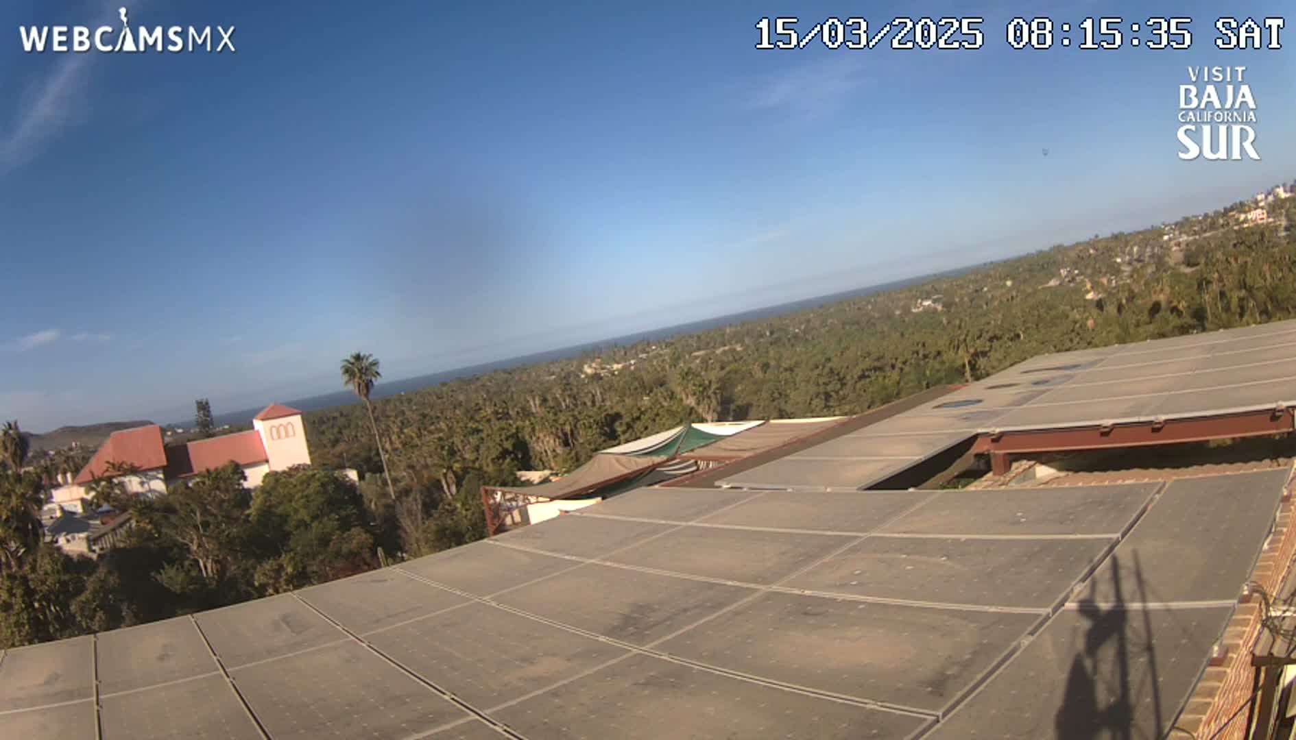 A rooftop view overlooking a coastal town under a clear blue sky, with a body of water visible in the distance.