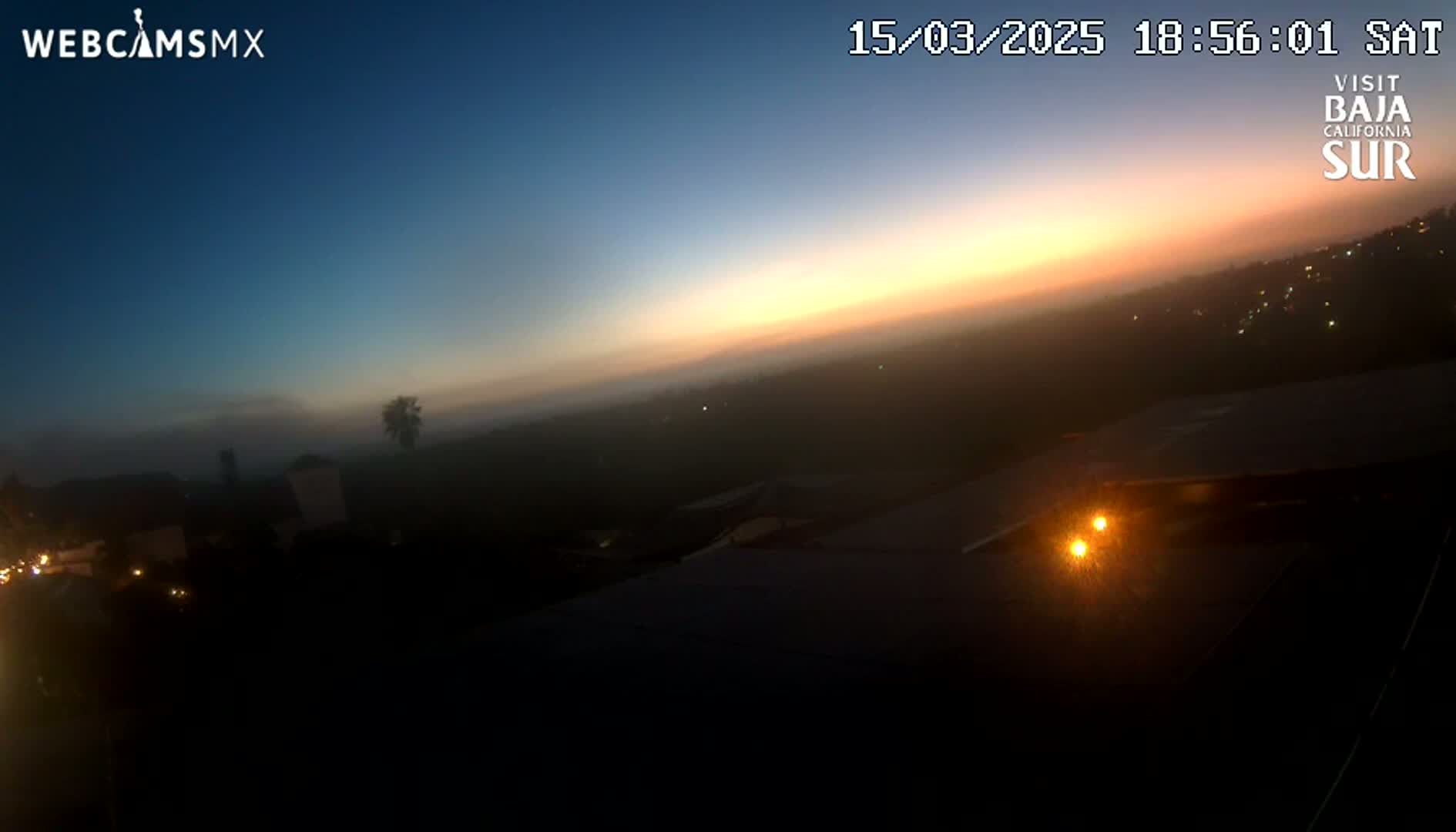 A hazy sunset over a dark landscape with a few distant lights visible.