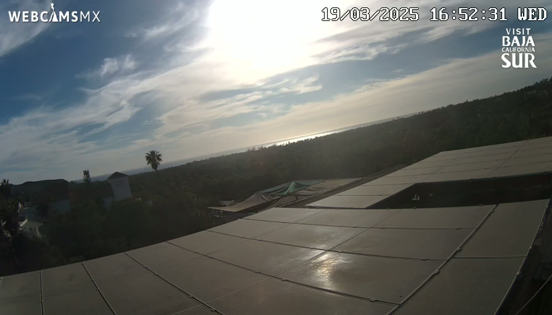 A partly sunny day overlooking a coastal landscape with a view of the ocean and a large expanse of solar panels in the foreground.