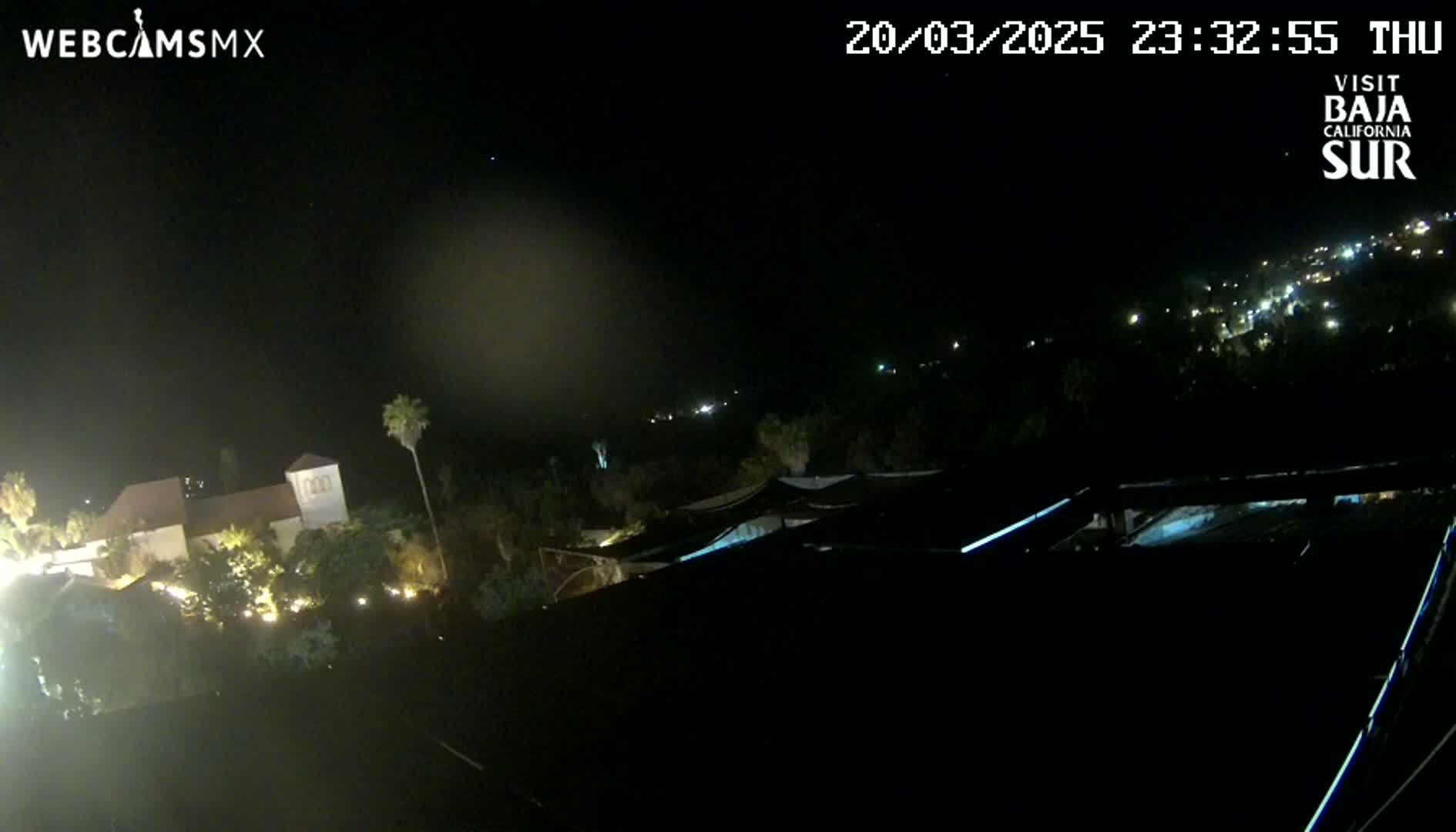 A nighttime, aerial view shows a building complex with lights on, palm trees, and a dark, starlit sky.
