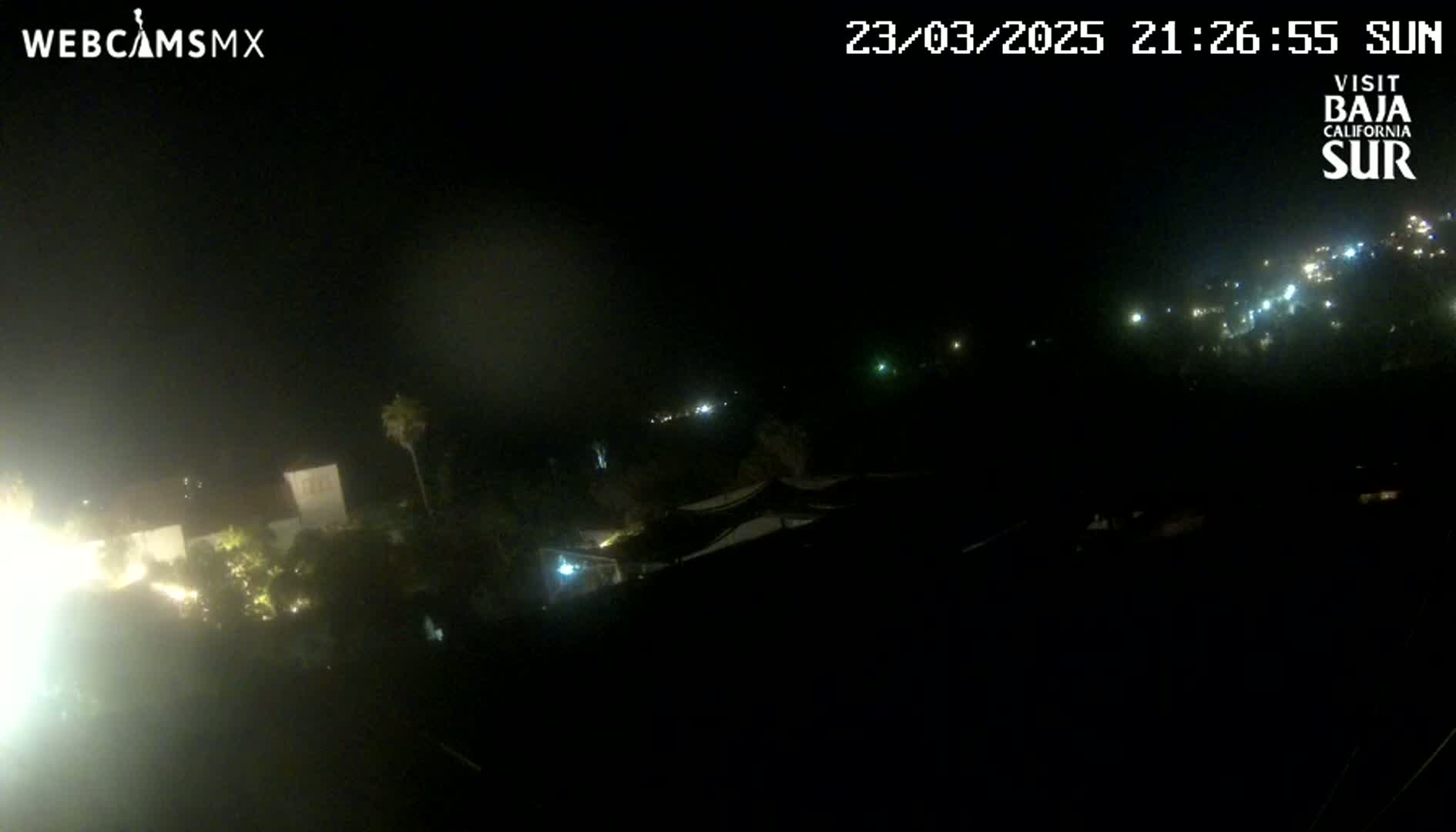 A nighttime long shot of a dimly lit town, partially obscured by darkness and haze.