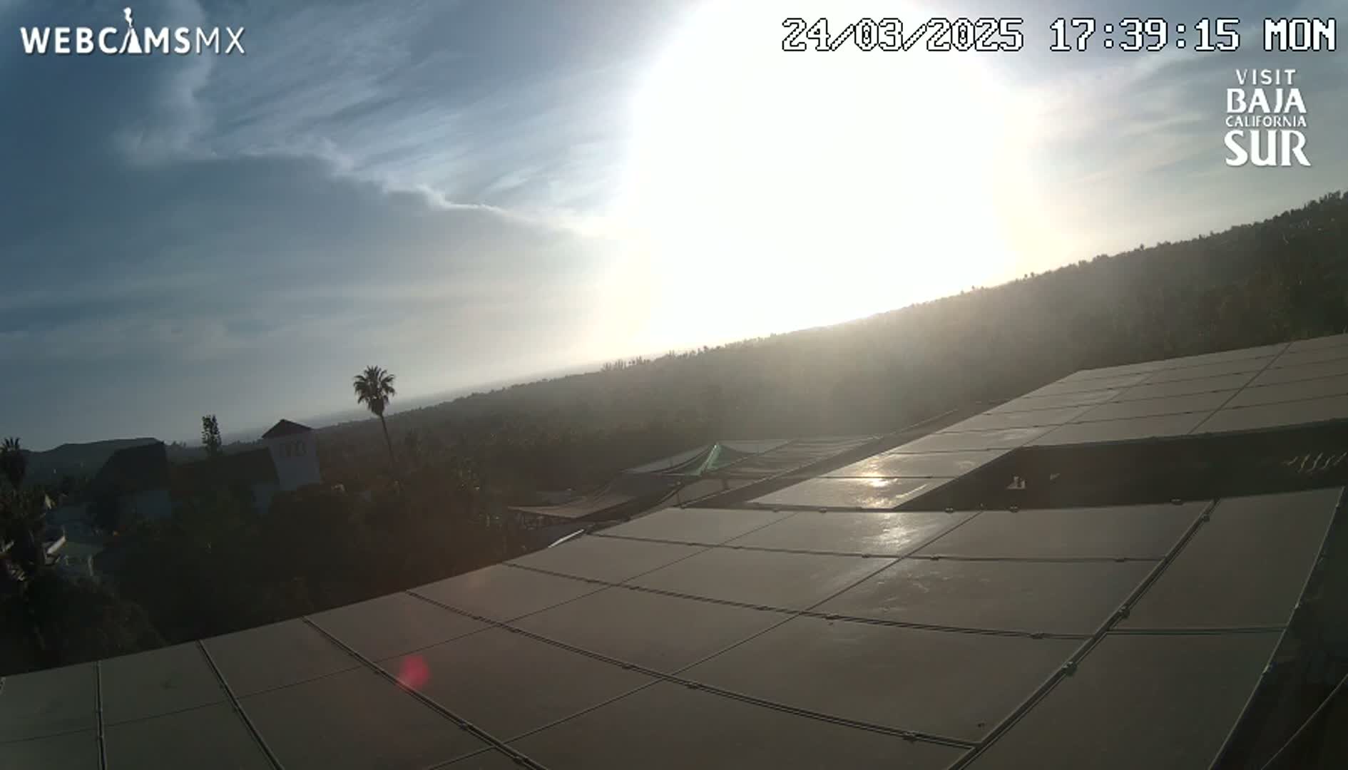 A mostly sunny, partly cloudy late afternoon view from a rooftop overlooking a hilly landscape with vegetation.
