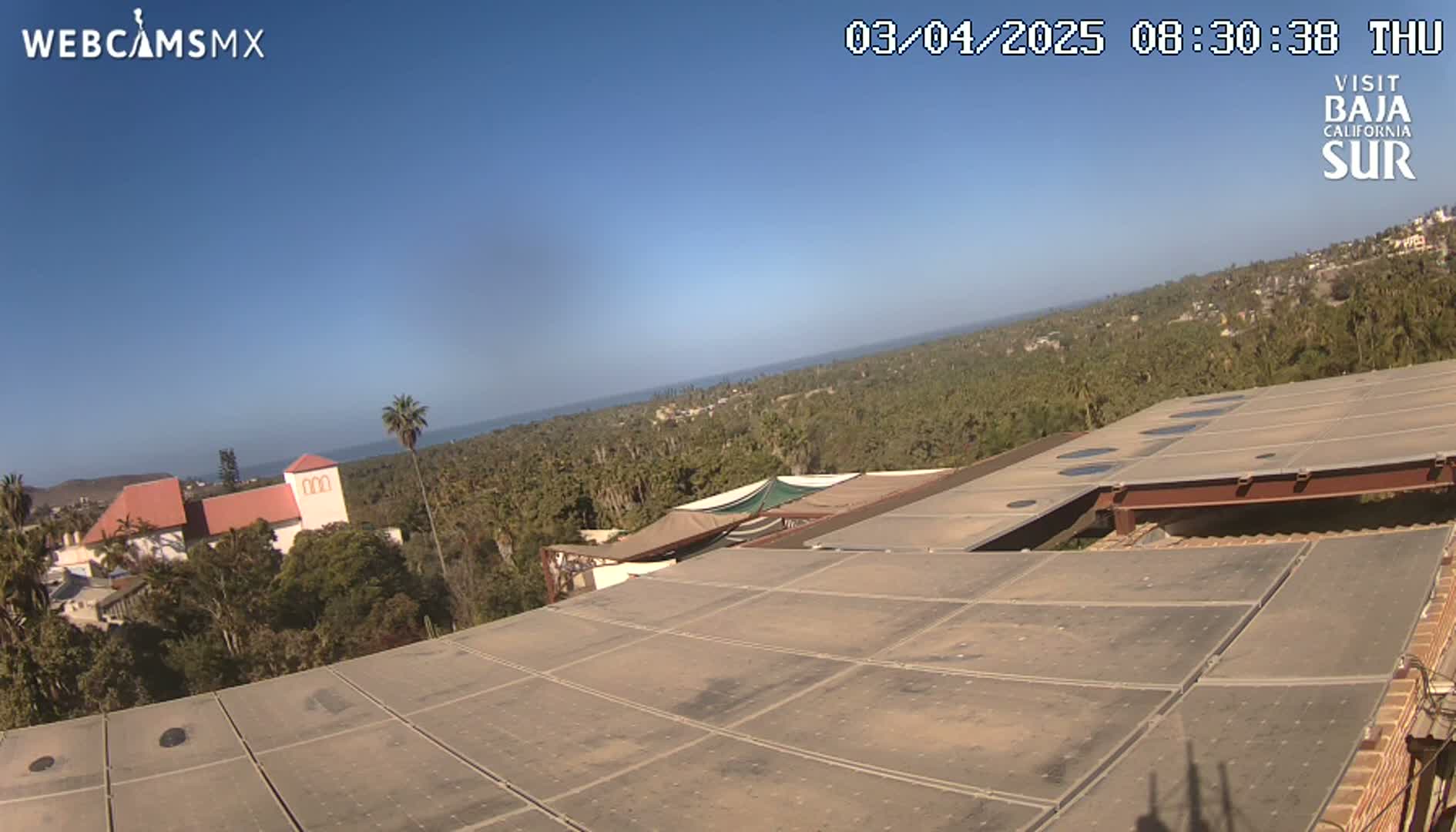 A rooftop view overlooking a coastal town and ocean under a clear blue sky.