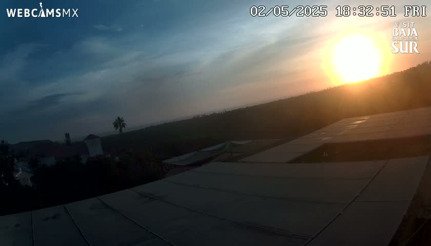 A sunset over a landscape of trees and buildings, viewed from a rooftop with a large, flat surface.