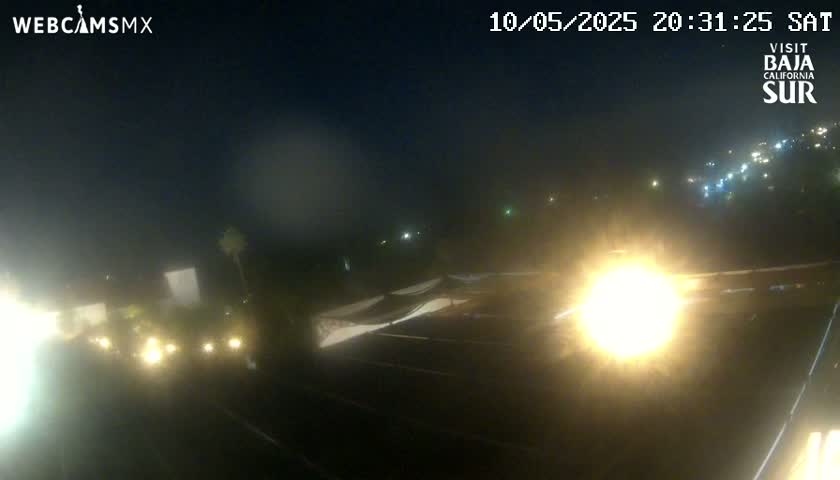 A nighttime, hazy view of a road with some vehicle lights visible, and a structure resembling a tennis court in the foreground.