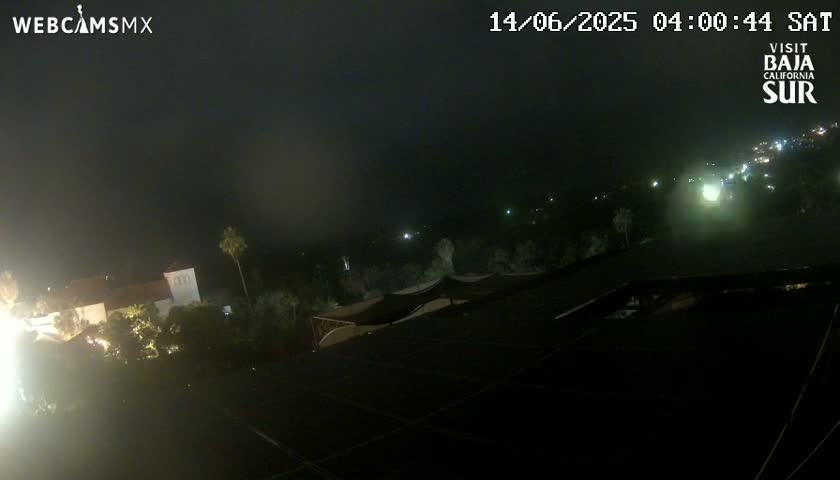 A nighttime aerial view of a dimly lit area with buildings and vegetation, under hazy or foggy conditions.