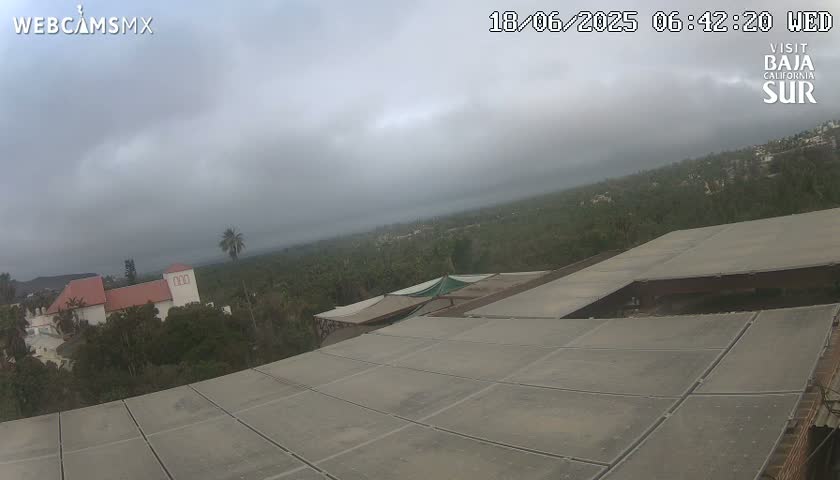A mostly cloudy view overlooking a building complex and a sprawling landscape of vegetation under an overcast sky.