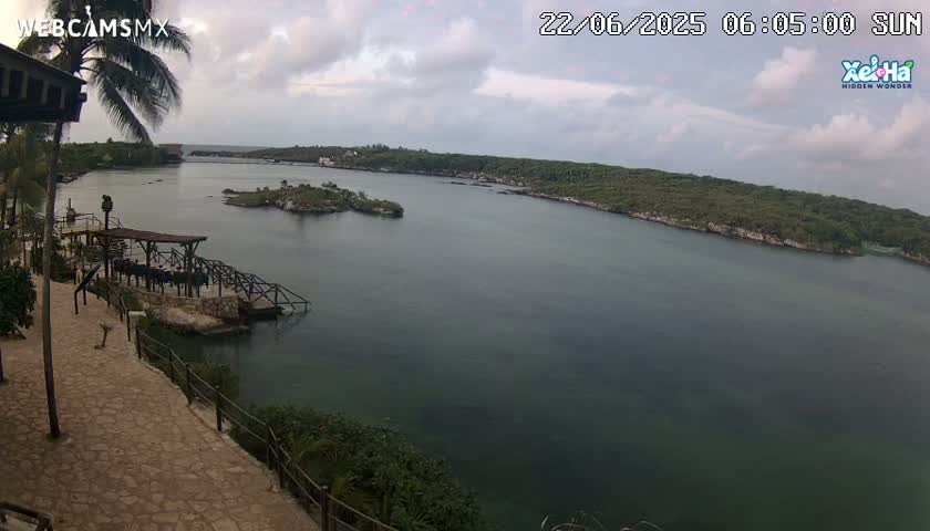 An overcast day reveals a tranquil bay with a small island and a stone walkway leading to a dock.