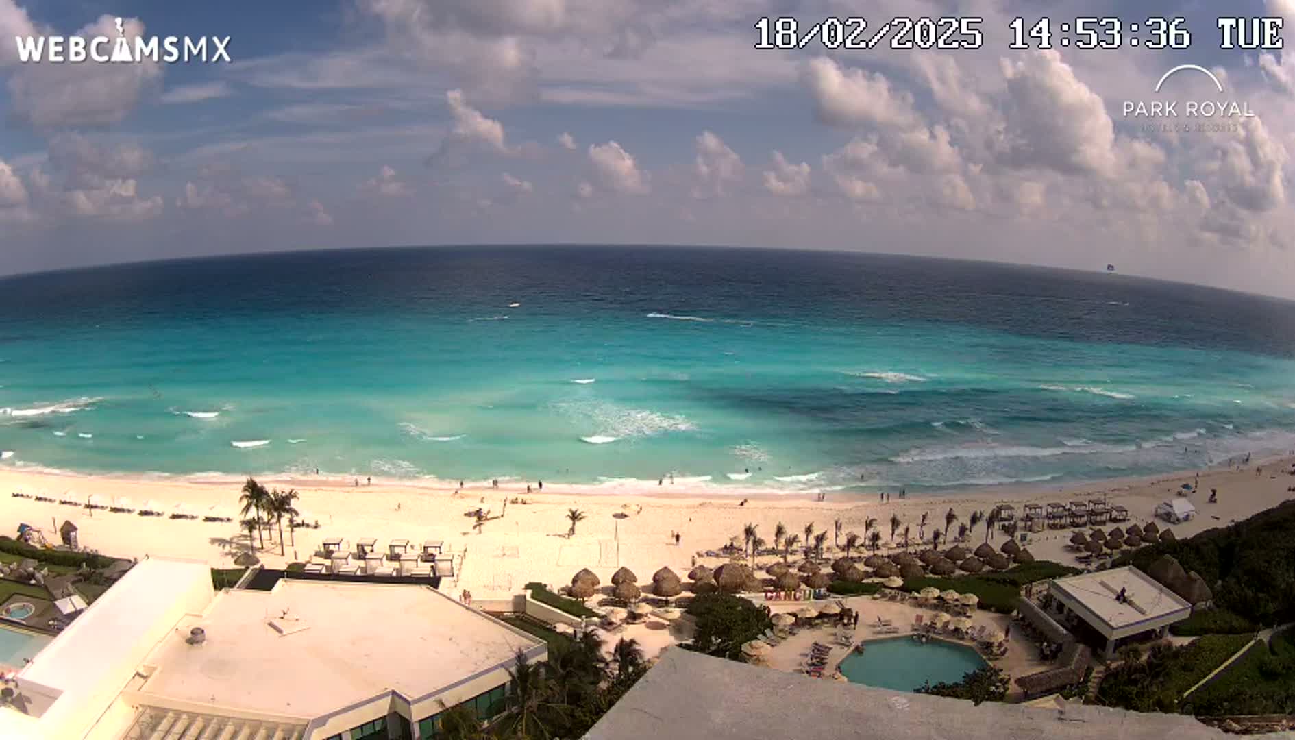 An aerial view shows a beach with turquoise water under a partly cloudy sky.