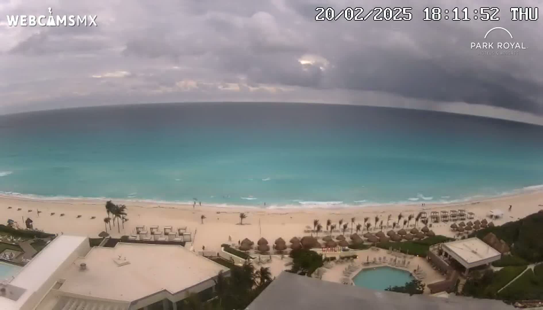 An aerial view shows a beach with turquoise water under a cloudy sky.