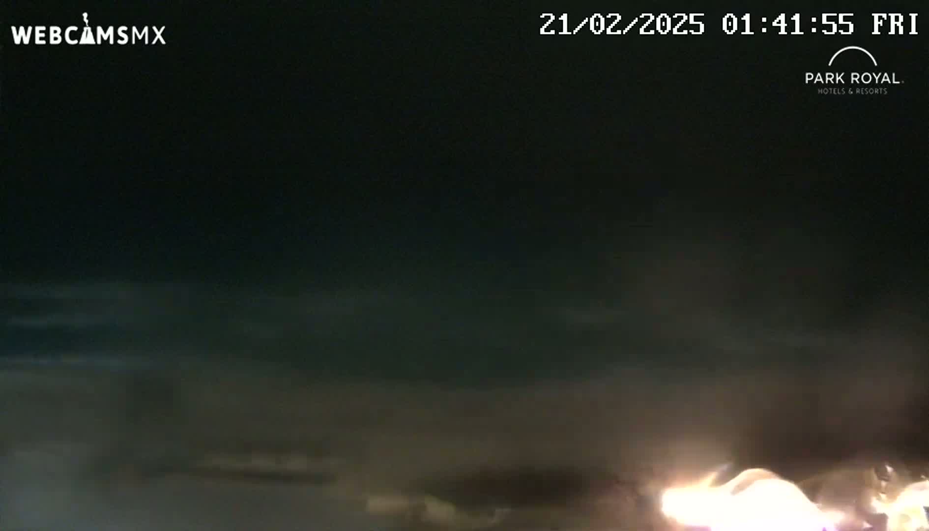 A nighttime, outdoor scene shows a bright light source at the bottom of the frame against a dark sky with faint clouds.