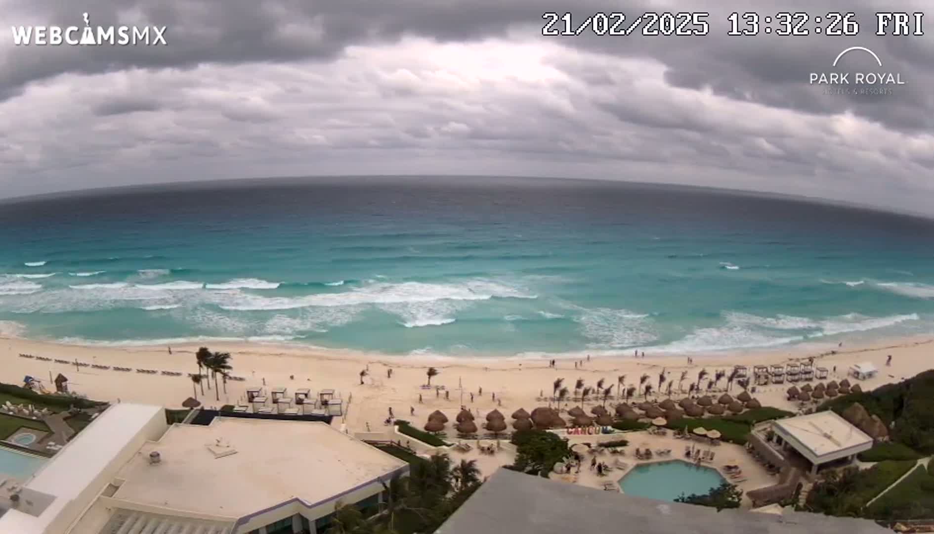An aerial view shows a beach with turquoise water and waves under an overcast sky.