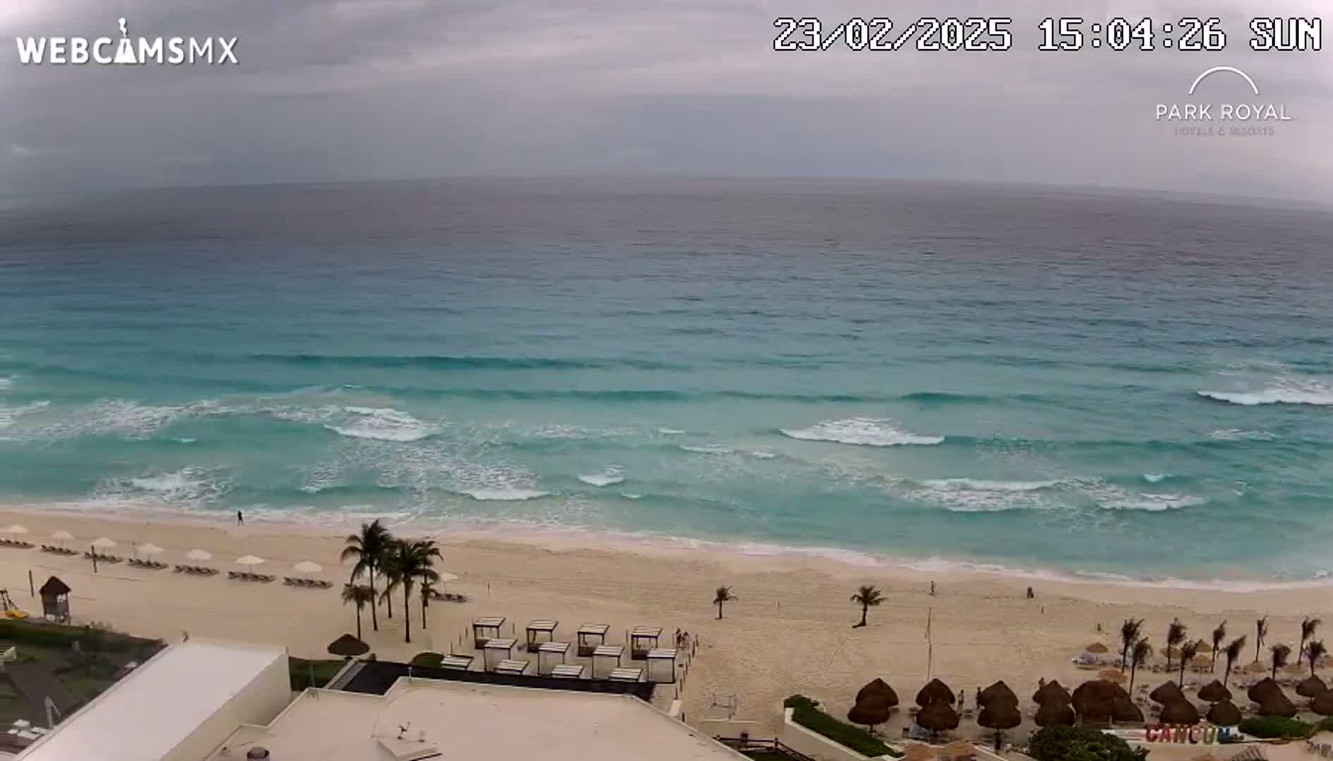 An aerial view shows a beach with calm waves under an overcast sky.