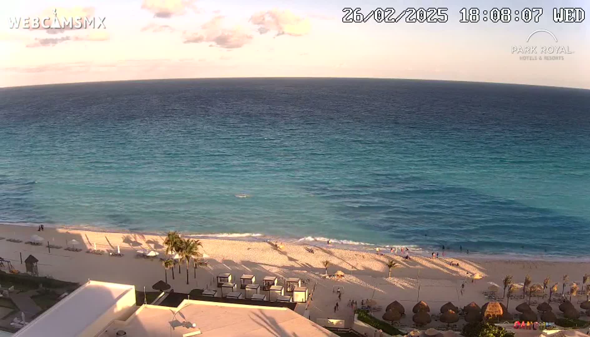 A beach with calm, turquoise water under a partly cloudy sunset sky.