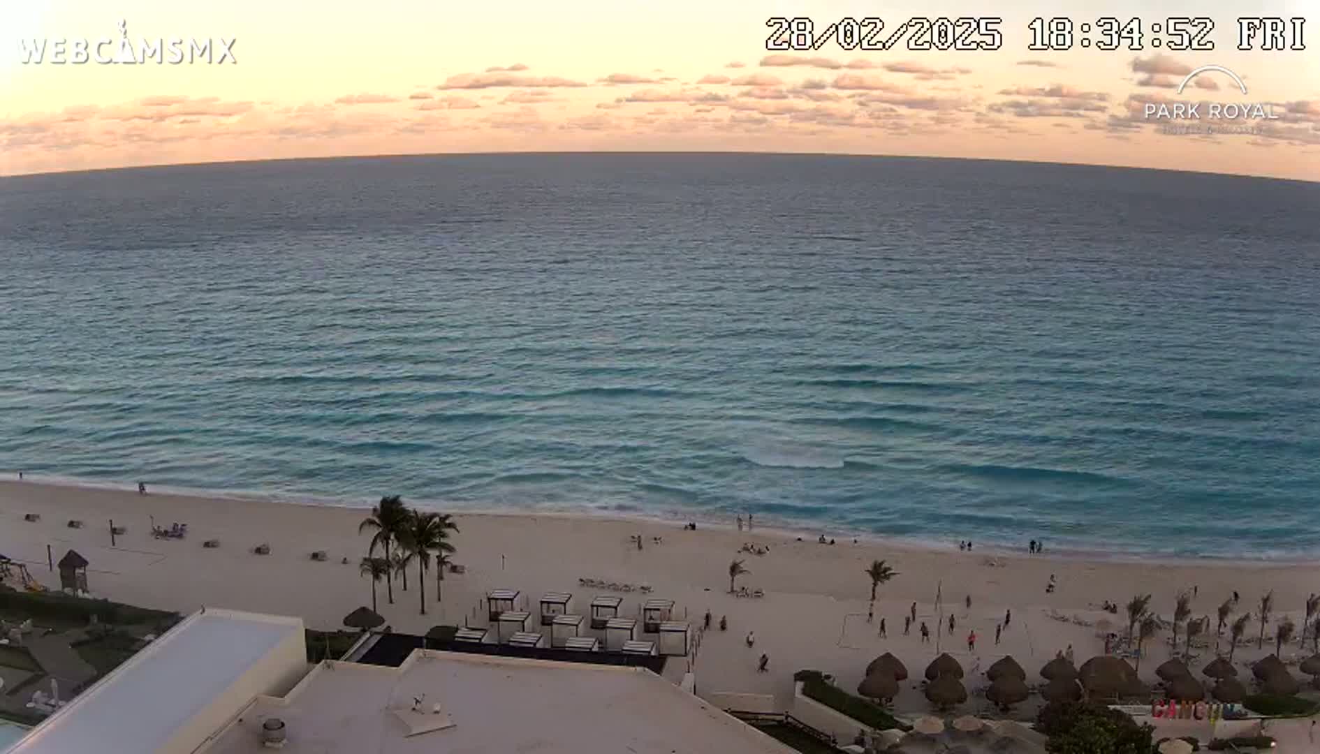 An elevated view shows a calm ocean at sunset with a sandy beach and resort amenities below.