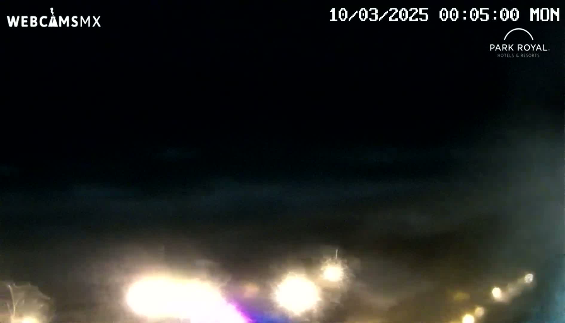 At night, under a dark, cloudy sky, hazy light from distant vehicles illuminates a dark landscape.