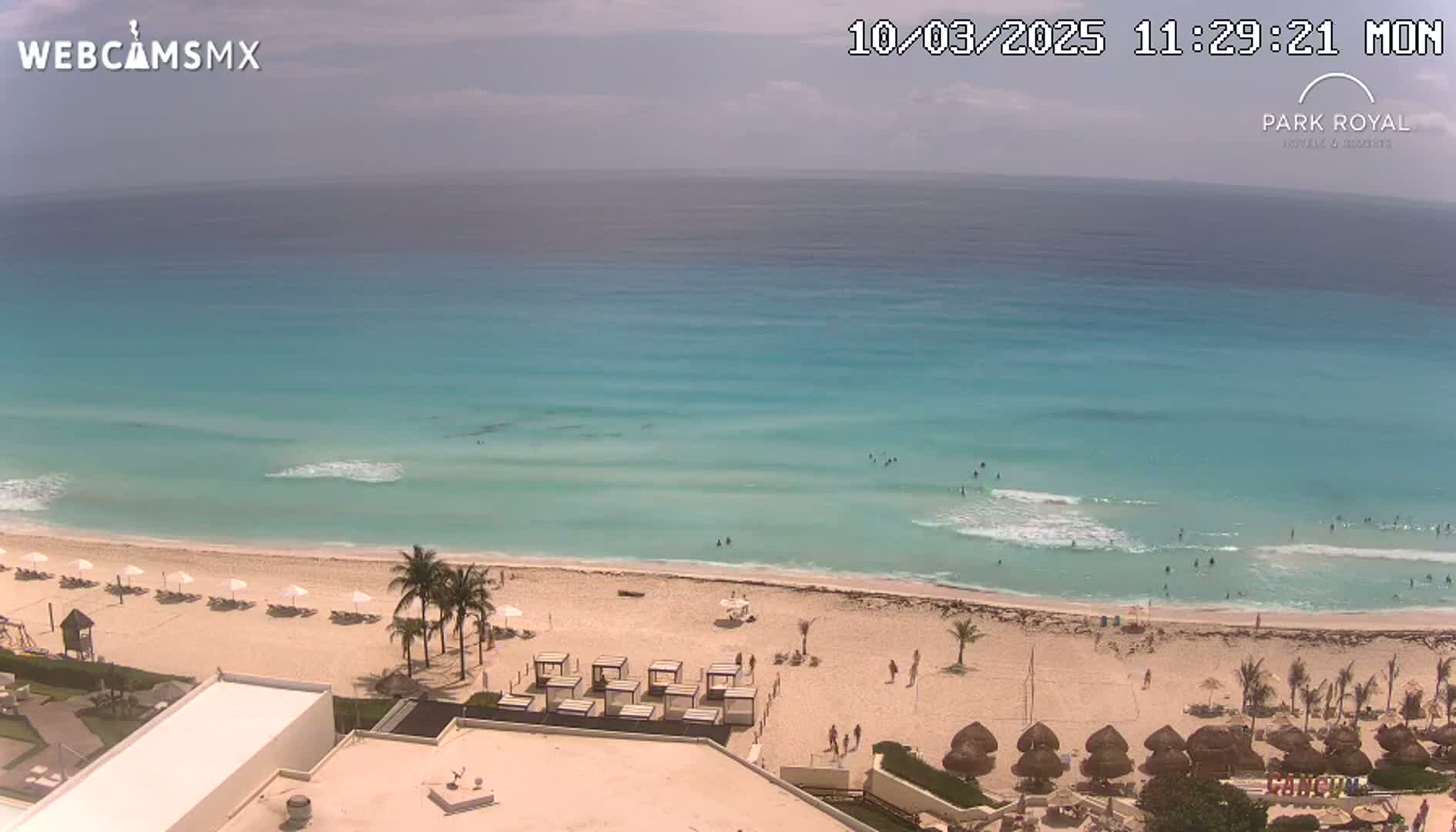 A mostly sunny day at a beach with turquoise water, white sand, and people swimming and sunbathing.