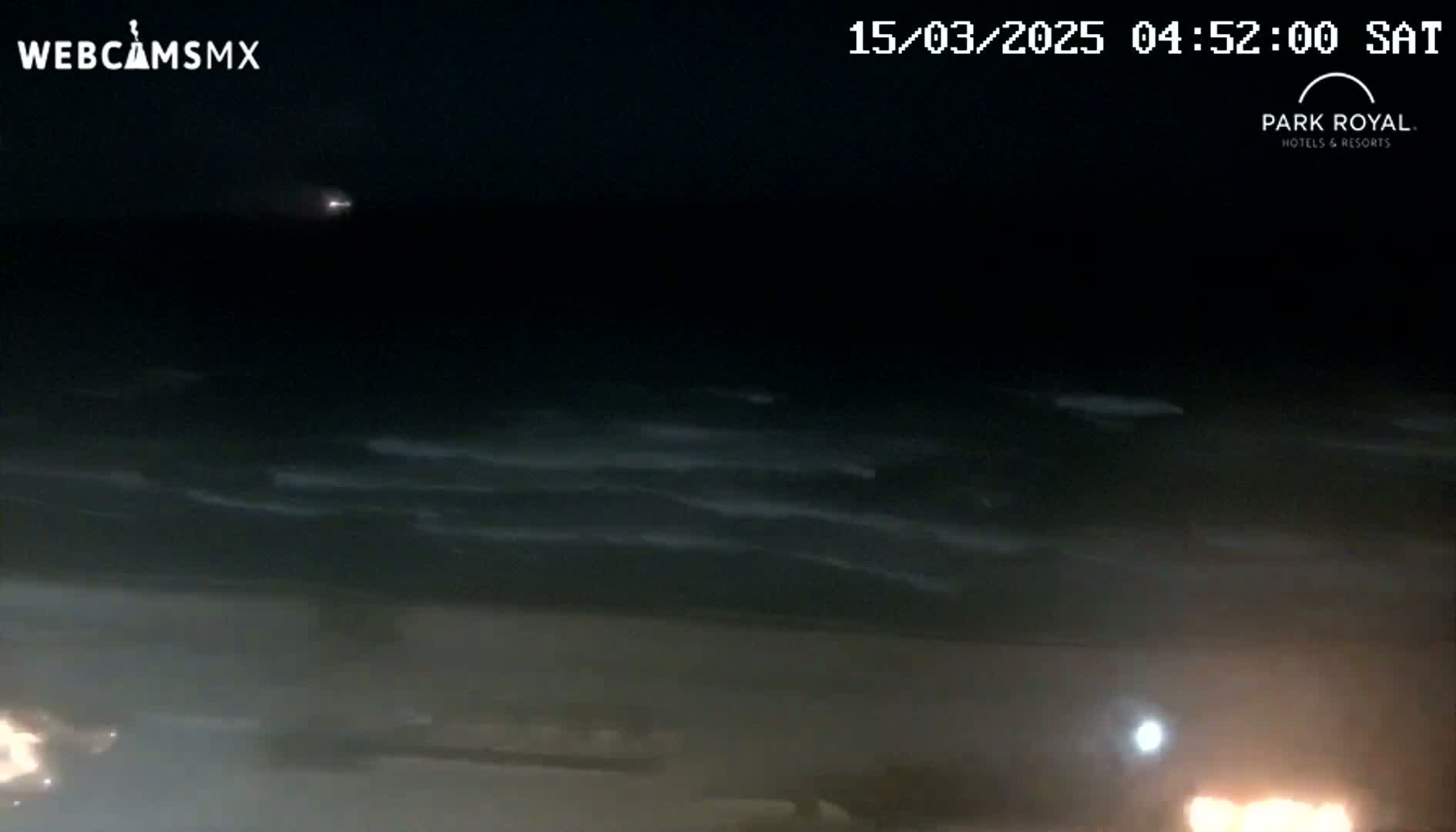 A dark, nighttime beach scene shows gently moving waves under a clear sky.