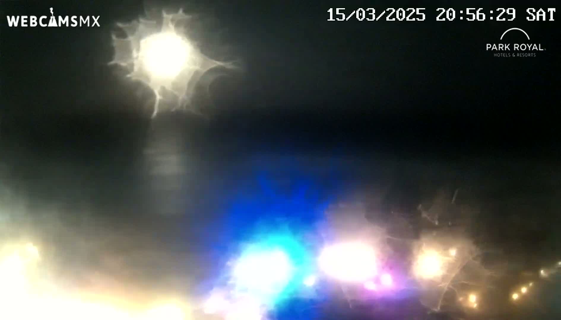 A nighttime outdoor scene shows blurry lights from vehicles and a bright light source obscured by what appears to be heavy rain or fog.
