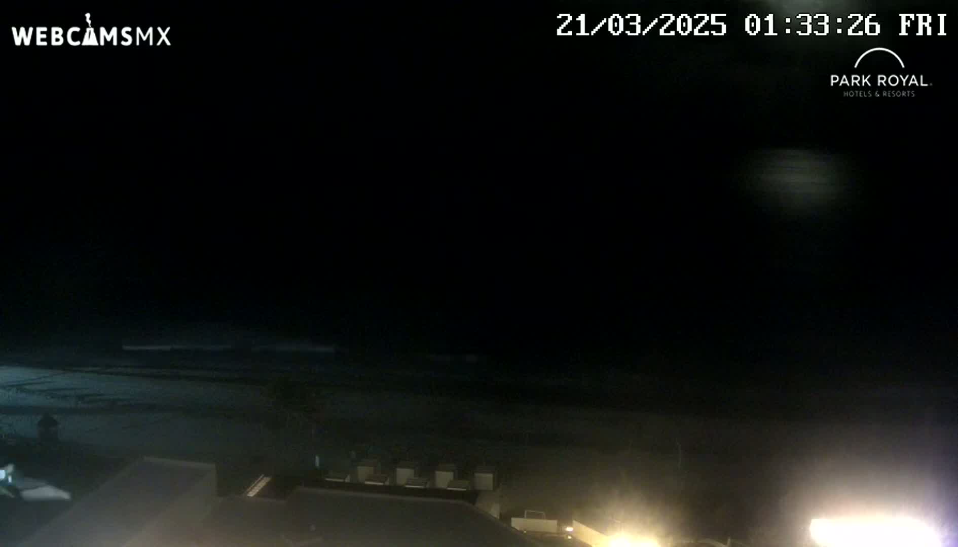 A nighttime view of a dark beach and ocean under a mostly clear sky, with some lights visible in the foreground.