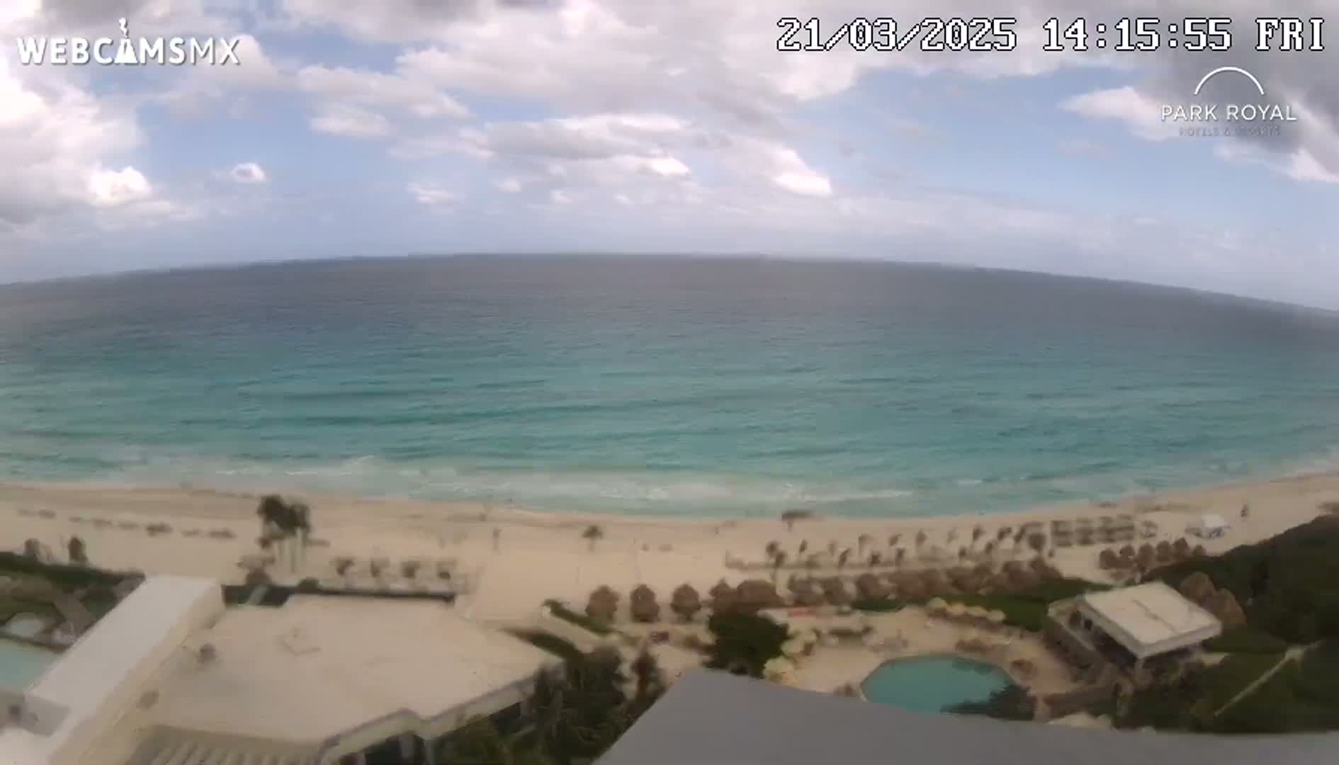 A partly cloudy day shows a beach with turquoise water, beach umbrellas, and a resort pool.